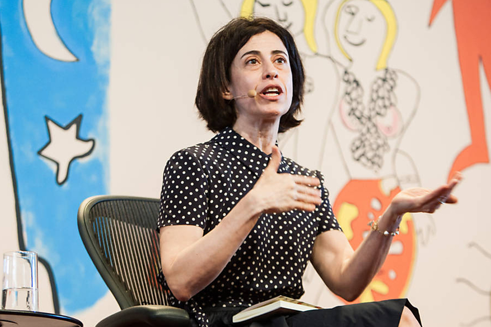 na foto, Fernanda Torres aparece dando uma palestra com microfone no rosto