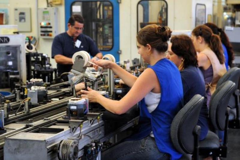 Foto mostra homens e mulheres trabalhando em uma fábrica. Imagem ilustra matéria sobre desigualdade salarial entre homens e mulheres.