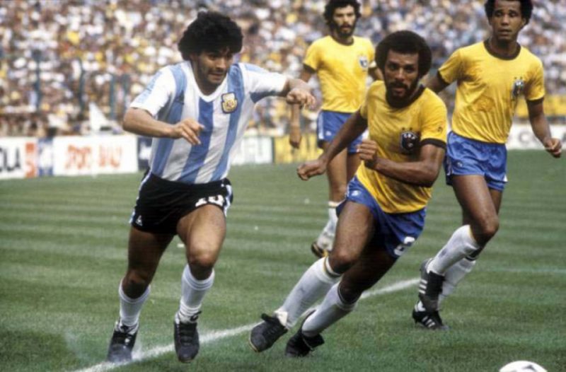 Rivalidade eterna. Na Copa de 1982 o Brasil levou a melhor: 3 x1. Maradona recebe a marcação do lateral Júnior, sendo observado pelo zagueiro Luisinho. Sócrates observa o lance. – Foto: (Foto: Divulgação)