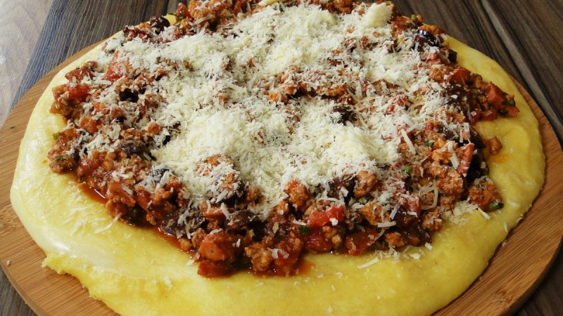 Foto de uma tábua com polenta mole, carne moída e queijo. 