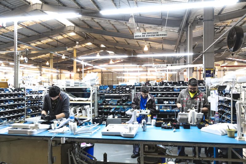 linha de produção de indústria, em uma mesa grande, três homens trabalham