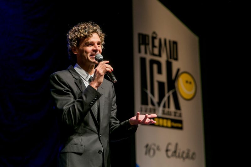 Guga Kuerten usa terno preto e fala em microfone e no fundo é possível ler prêmio IGK