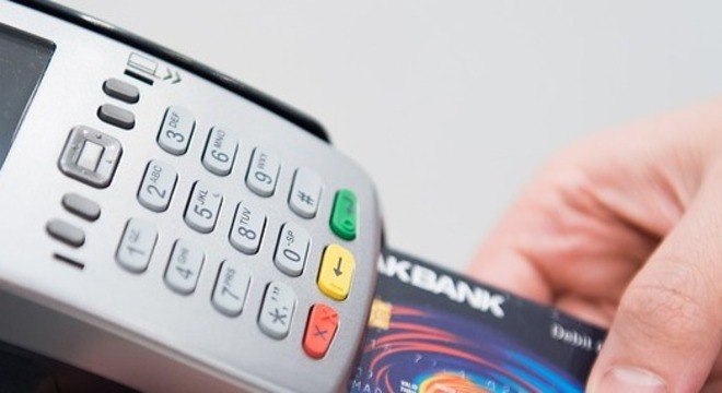 Na foto aparece uma máquina de cartão de crédito com uma pessoa inserindo para fazer um pagamento.