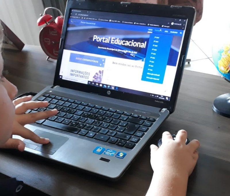 Na imagem aparece uma criança usando um computador. Na tela do computador está aberto um site de atividades pedagógicas.