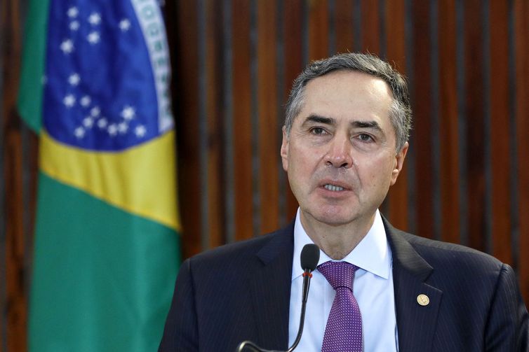 Ministro Barroso e ao fundo uma bandeira do Brasil