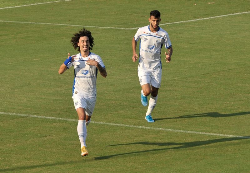 Valdívia está vestindo camisa branca do Avaí e comemorando gol pelo Avaí. Ao lado, aparece Lourenço correndo
