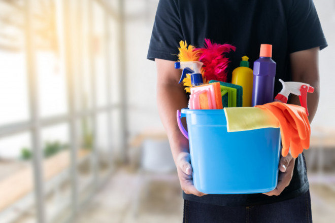 Pessoa segurando balde azul com diversos produtos de limpeza 