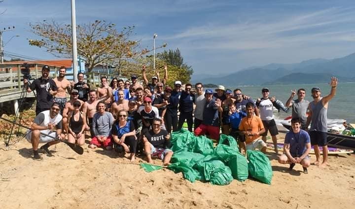 Jovens e adultos estão na praia com sacos de lixo, com objetos que recolheram da praia