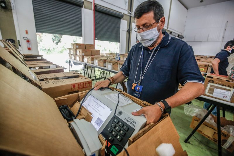 Um mesário retira uma urna. há caixas com outras urnas ao redor