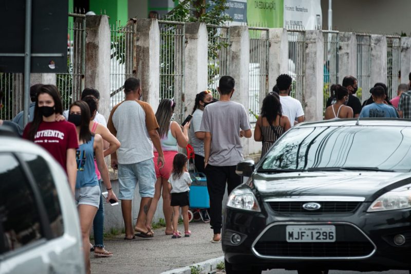 Pessoas em fila para votar em Florianópolis. Usam máscara. Aparecem dois carros na foto