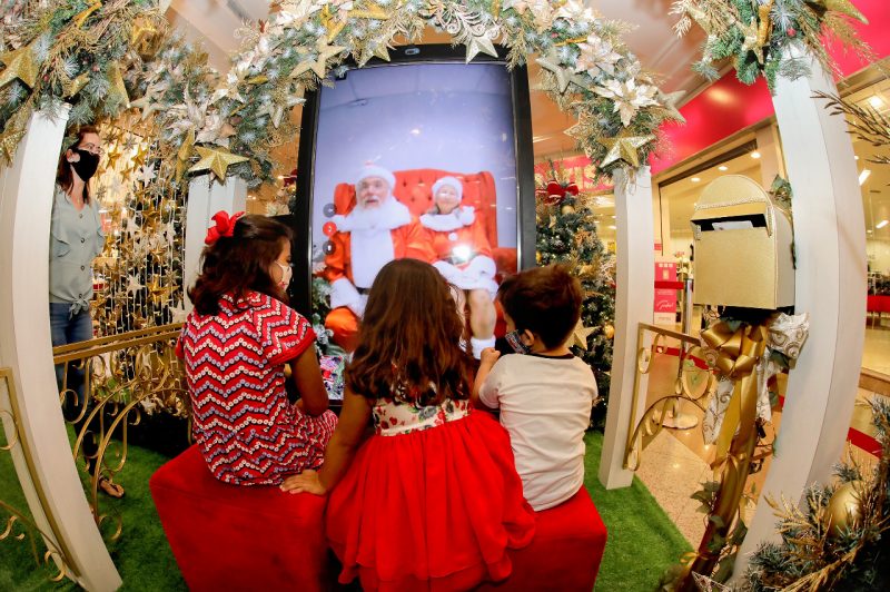Crianças olham o totem virtual com Papai Noel e Mamãe Noel
