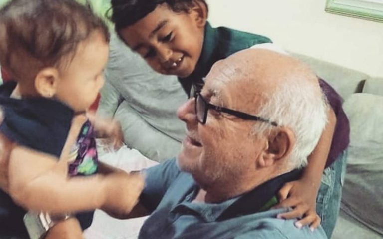 Fotgrafia de Renaud com os netos. Ele sorri levantando uma das crianças com os braços. 