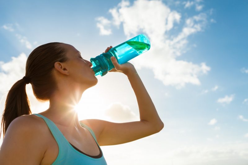 Cuidados no verão: Mulher tomando água em garrafinha durante temperaturas mais altas 