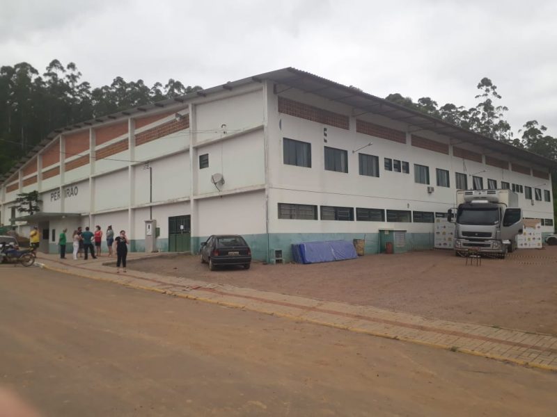 Ginásio branco com verde. Aparecem pessoas ao lado