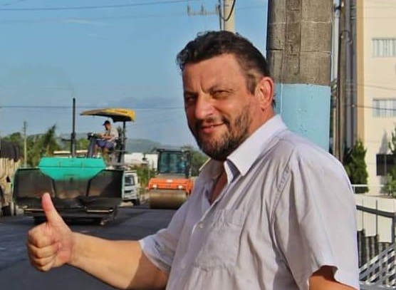 Humberto Pessatti aparece nno meio de um rua que está sendo pavimentada. Ele faz sinal de joia com a mãe.