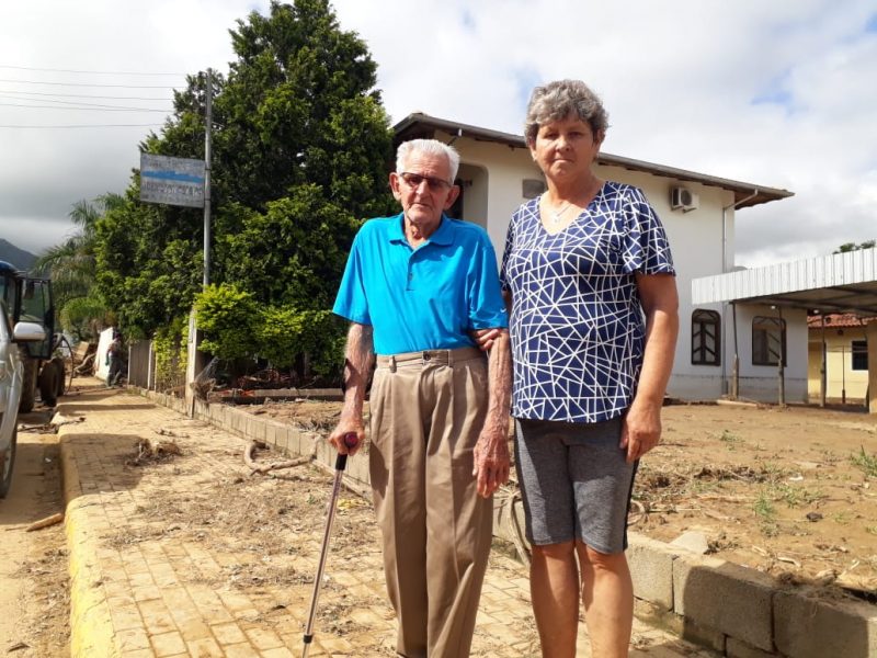 Moradores em pé ditante da tragédia. Um senhor com bengala e cabelo branco e uma senhora