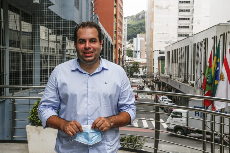 João Cobalchini (DEM), de camisa azul, segura uma máscara nas mãos e sorri