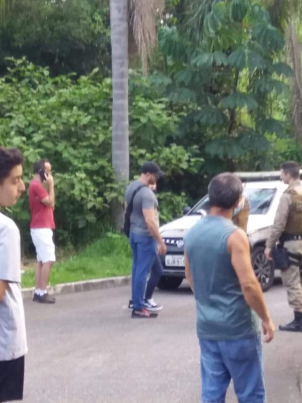 Pessoas em frente a um carro da PM perto do matagal de onde encontraram a cabeça