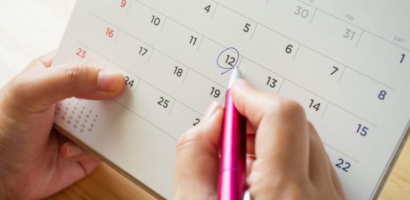 uma pessoa segurando um calendário, em uma das mãos segurando uma caneta e circulando o número 12 no calendário da data de nascimento 