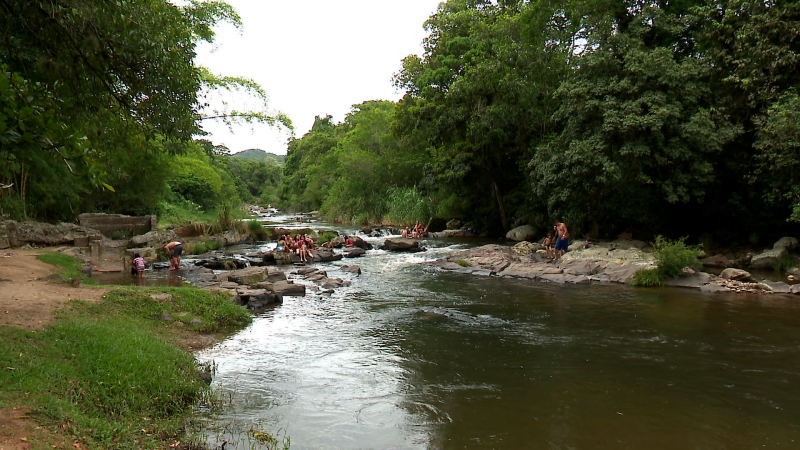 Foto de um rio com algumas pessoas tomando banho. O entorno é todo de vegetação.