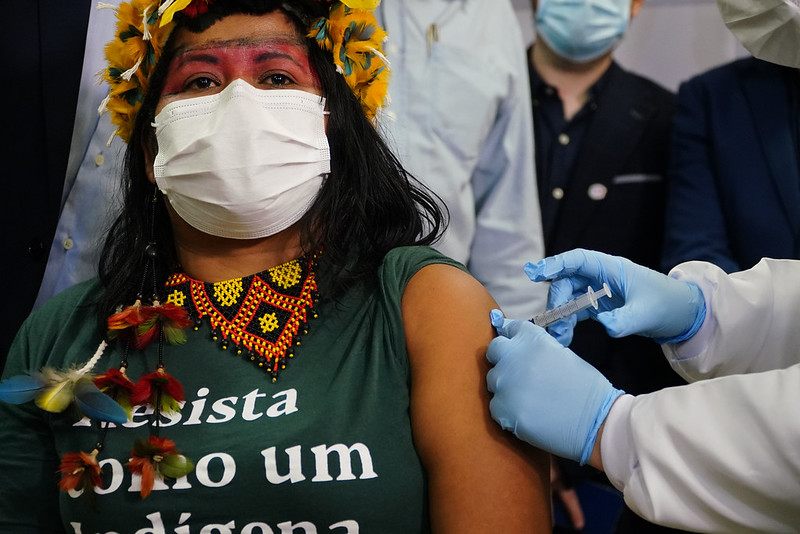 A primeira indígena a ser vacinada no Estado, Ela olha para a câmera e está de máscara enquanto recebe a vacina
