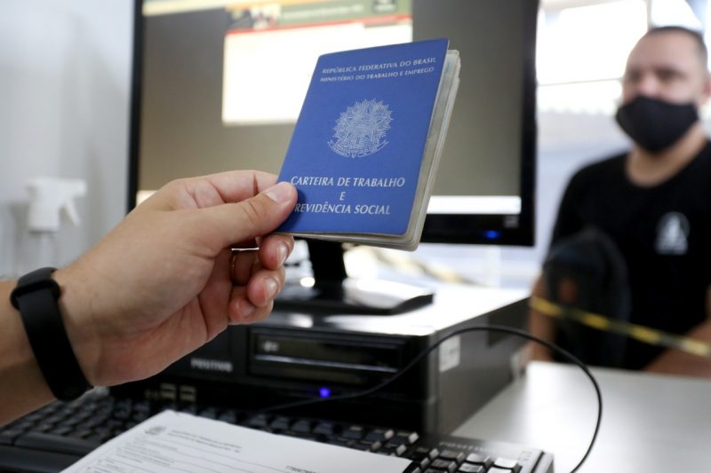 na foto aparece um homem que pede seguro-desemprego e atendente com carteira de trabalho na mão