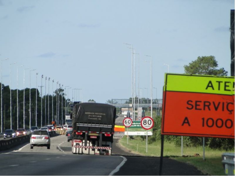 Rodovia BR-101 com trânsito de veículos e placas de atenção