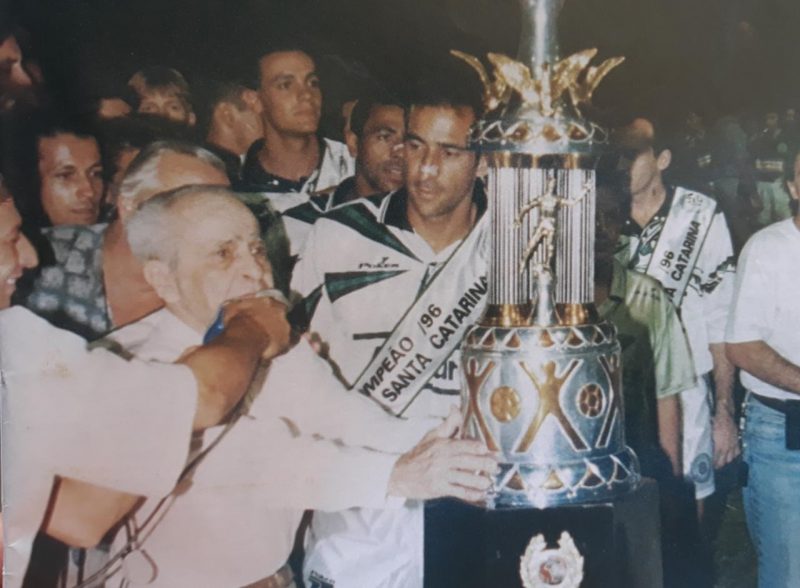 Em 1996, o Figueirense conquistou a o t&iacute;tulo da Copa Santa Catarina. Por ironia do destino, o trof&eacute;u levou o nome de um dos maiores &iacute;dolos da hist&oacute;ria do rival Ava&iacute;, o ex-atacante Saul Oliveira, que aparece na foto entregando o trof&eacute;u para o capit&atilde;o do alvinegro, Vin&iacute;vius Eutr&oacute;pio, hoje treinador do Joinville, e&nbsp; campe&atilde;o da mesma Copa SC na semana passada. No canto direito, aparece o saudoso rep&oacute;rter Evaldo Filho – Foto: Memorial Alvinegro/ND