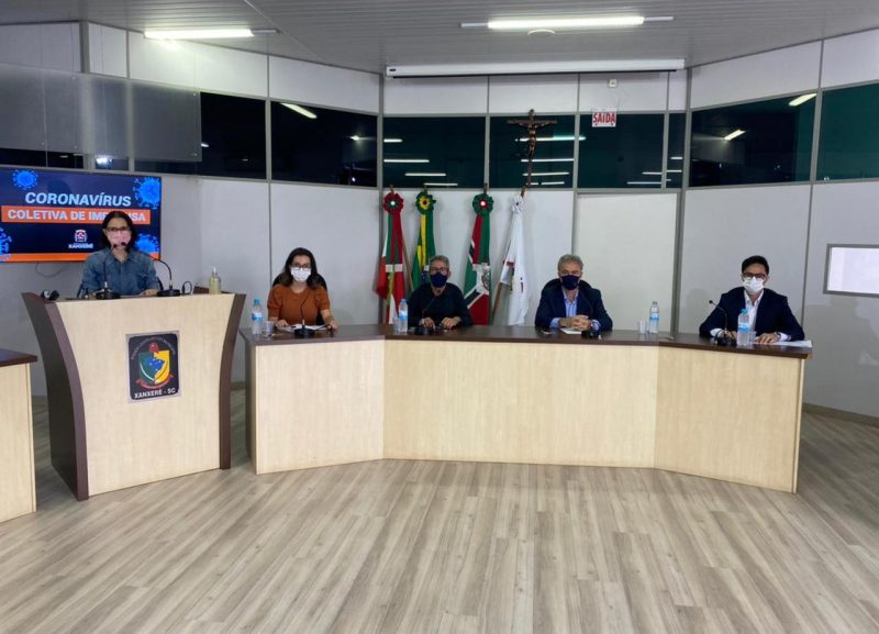 Coletiva de imprensa realizada para atualização das medidas de combate à Covid-19 em Xanxerê, Na imagem aparece cinco pessoas sentadas em um auditório. Entre eles está o prefeito de Xanxerê Oscar Martarello e demais autoridades da saúde e de segurança do município. 