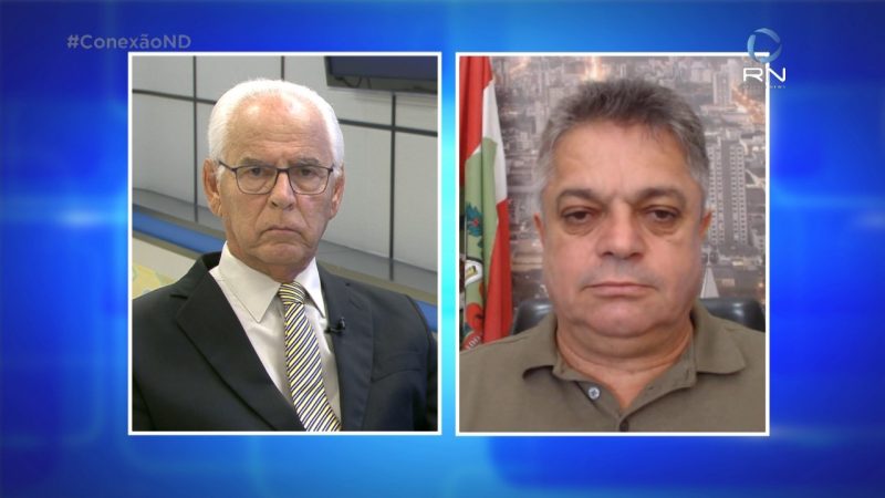 Moacir Pereira na esquerda, vestido com terno e gravata listrada; Prefeito de Chapecó na direita, com camisa polo marrom e margem azul na imagem