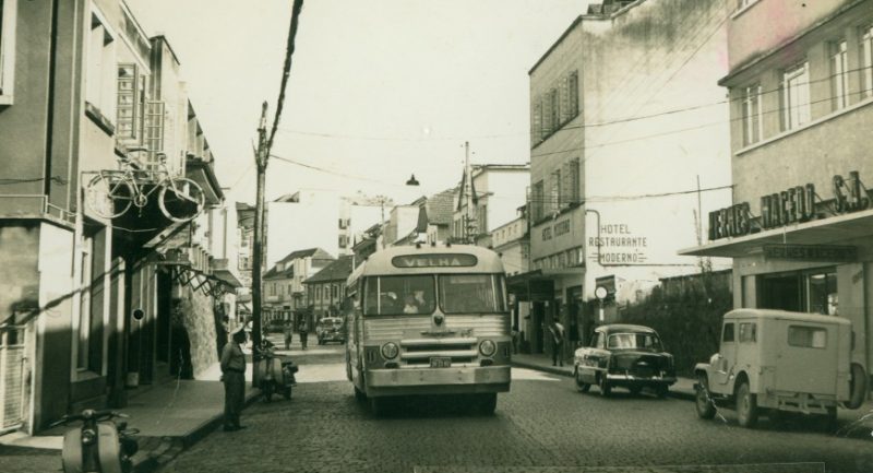 Nos anos de 1960 e 1970 começaram efetivamente as construções verticais com os edifícios Albor, Catarinense e Impala, entre outros. O prédio da antiga Moellmann passou por mudança e adquiriu ares de estilo enxaimel. Na década de 1970, na gestão do prefeito Renato de Mello Vianna, foi criada a lei que estimula a adaptação da arquitetura enxaimel para fortalecer o setor turístico. Muitos proprietários de casas ao longo da rua adotaram essa iniciativa. Naquele período, já se podia observar o congestionamento de veículos na rua em decorrência dos ônibus que chegavam à antiga rodoviária, localizada na rua 7 de Setembro. Até 1973, o tráfego era em mão dupla e nesse ano passou a sentido único de circulação (sentido Velha/Garcia). Em 1977, o transporte coletivo foi retirado definitivamente da Rua XV. – Fonte e foto: Fundação Cultural de Blumenau / Arquivo Histórico José Ferreira da Silva