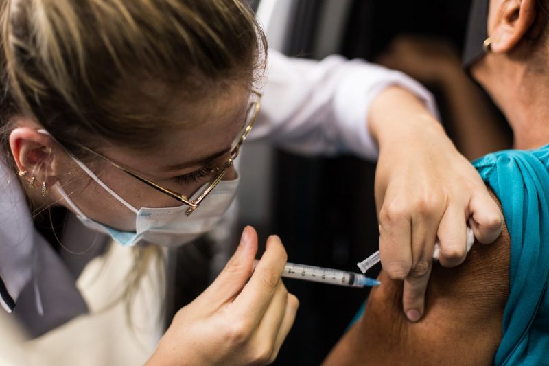 Enfermeira aplica vacina no braço de idoso