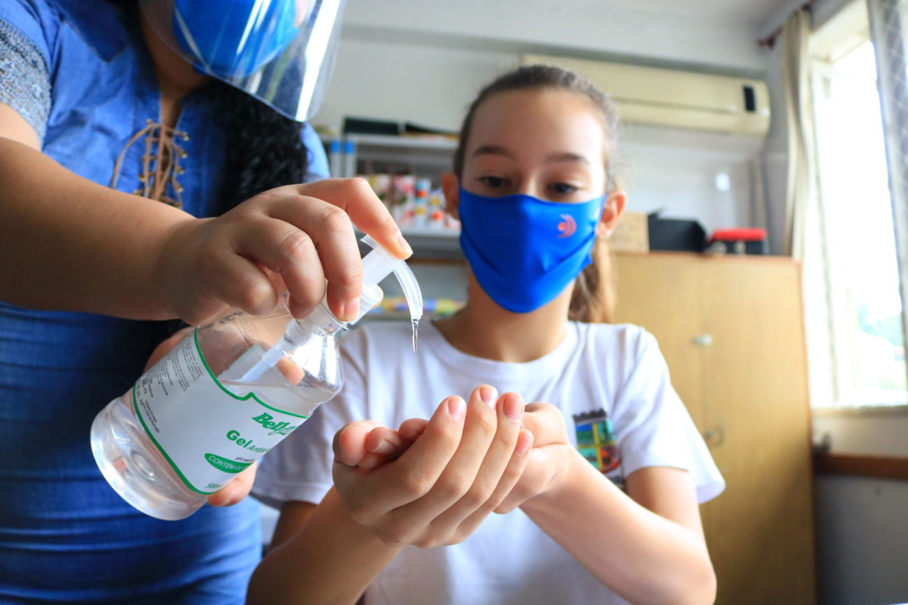 menina com máscara colocando alcool em gel