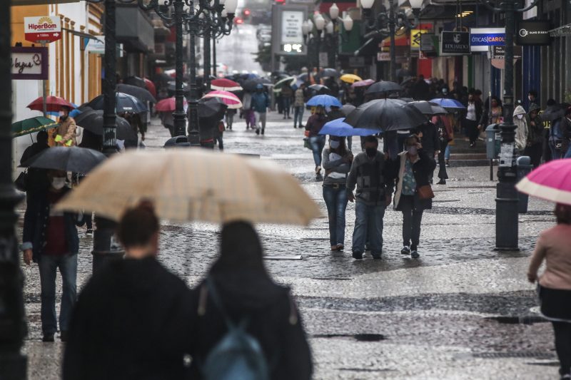 Imagem mostra pessoas em rua do Centro de Florianópolis com guarda-chuvas