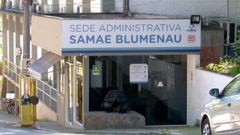 Samae Blumenau Imagem mostra fachada de prédio do Samae de Blumenau. É possível ver também um carro, motos e janelas do prédio