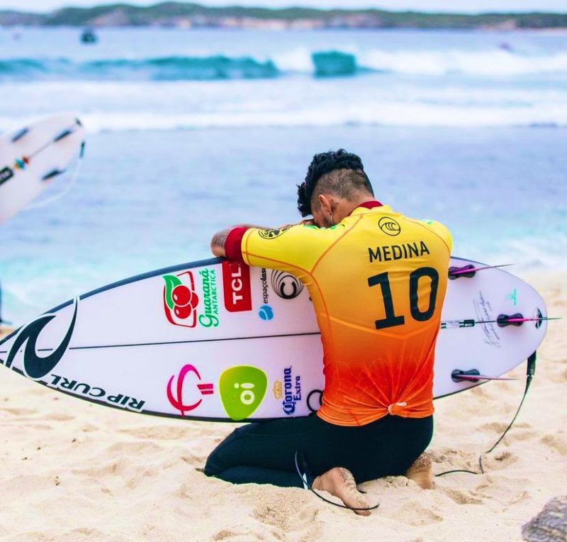 surfista Gabriel Medina ajoelhado com uma prancha