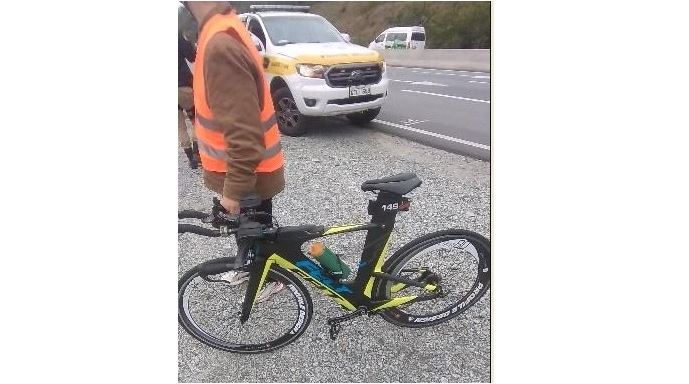 Imagem mostra homem segurando bicicleta preta e com detalhes amarelos e uma viatura da PMRv no fundo