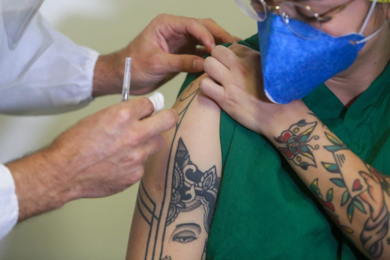 Imagem mostra pessoa limpando o braço da pessoa para aplicar a dose da vacina 