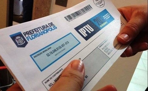 Duas mãos segurando o carnê do IPTU de Florianópolis