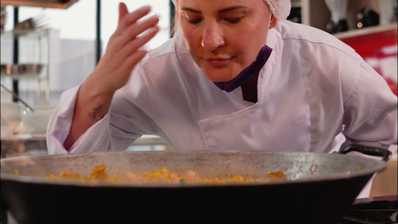 Paula não resiste ao aroma das carnes e temperos sendo preparados na paellera. – Foto: Três Oitavos Filmes/Reprodução