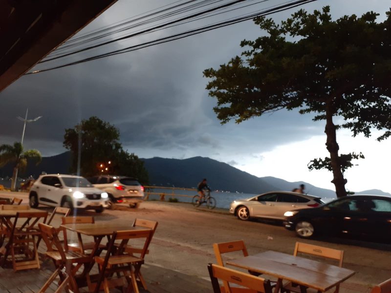 Imagem mostra nuvens se formando e em primeiro plano mesas e cadeiras na Lagoa da Conceição