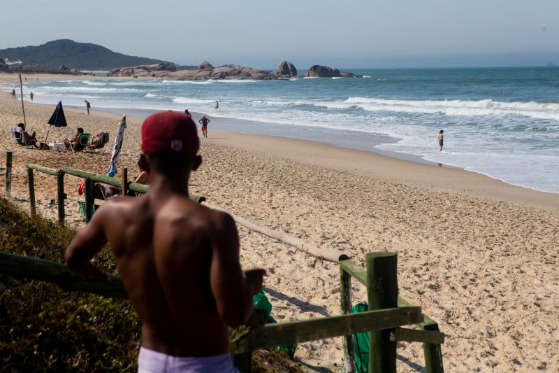 Imagem usada para representar o calor mostra um homem de costas usando um boné vermelho e no fundo a praia e a areia