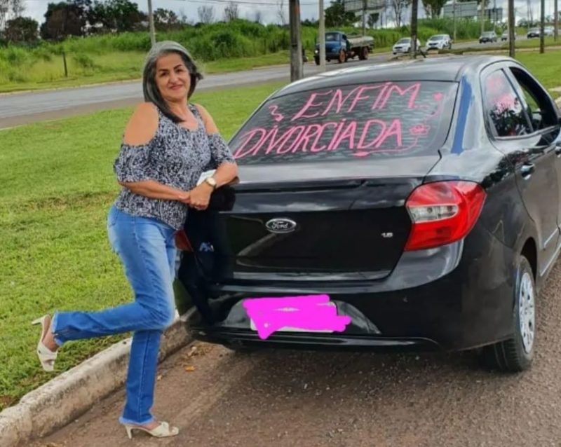 Mulher ao lado do carro preto escrito enfim divorciada no vidro do carro