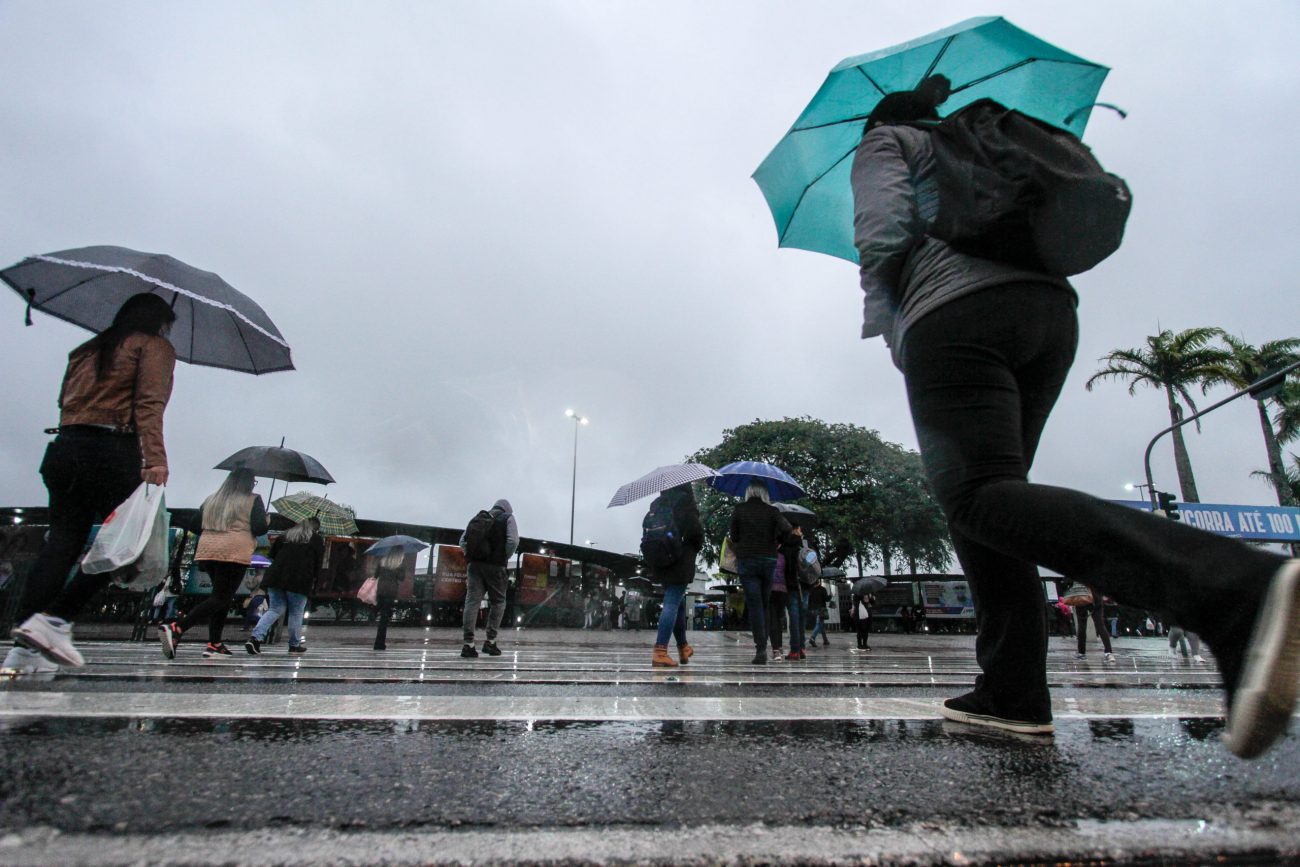 Na imagem aparece pessoas com guarda-chuva por conta de chuvas causada por uma intensa massa de ar quente e seco.