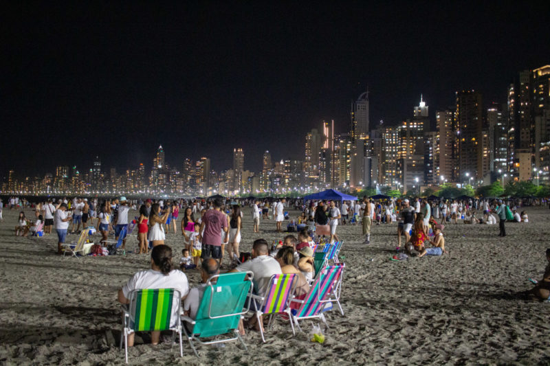 Imagem mostra pessoas sentadas em cadeiras na praia de Balneário Camboriú