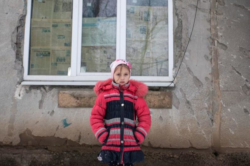 Menina posa em frente a parede danificada pelos ataques hist&oacute;ricos no Leste Europeu – Foto: Aleksey Filippov/UNICEF/Divulga&ccedil;&atilde;o