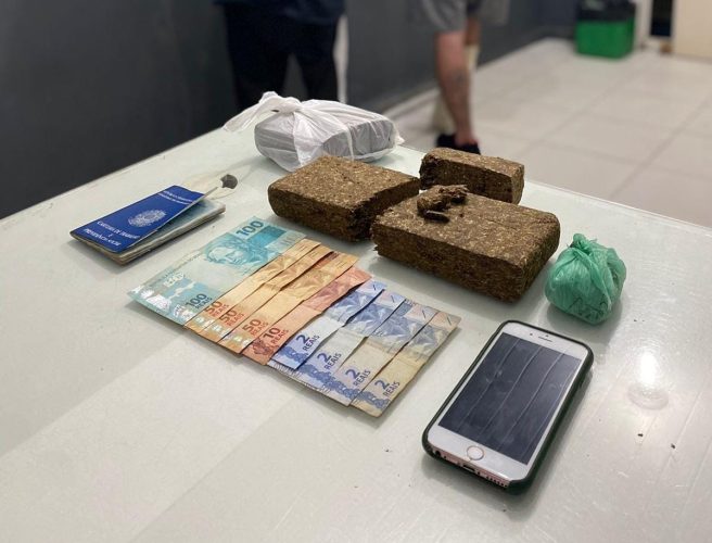 A imagem mostra dinheiro, drogas, celular e uma carteira de trabalho na delegacia