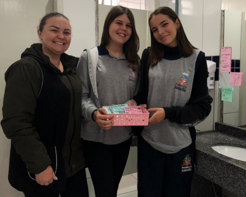 Alunas seguram os absorventes descartáveis arrecadados na escola