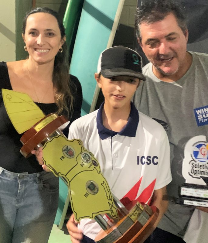 Davi entre os pais, Paula e Alexandre d’Eça Neves, ostentando mais um troféu de campeão sul-brasileiro de vela Optimist &#8211; Foto: Divulgação/ND