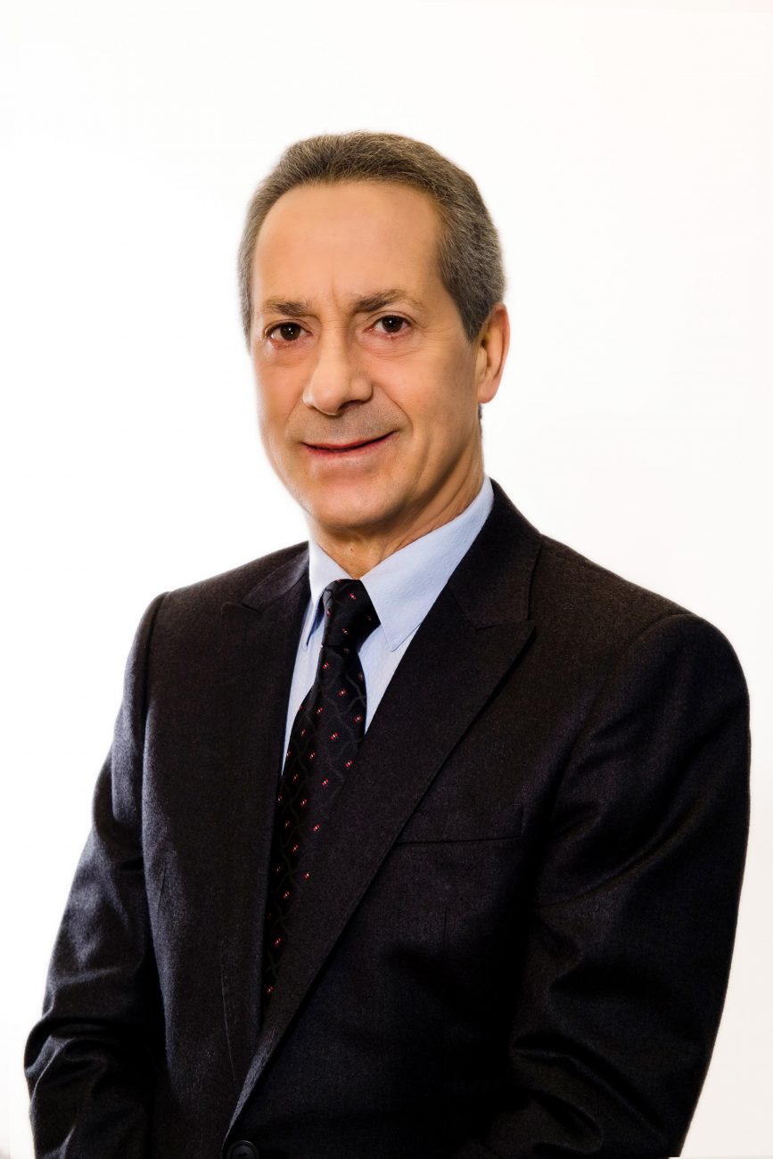 Senhor caucasiano, Neivor Canton, de terno preto, sob fundo branco, sorrindo 